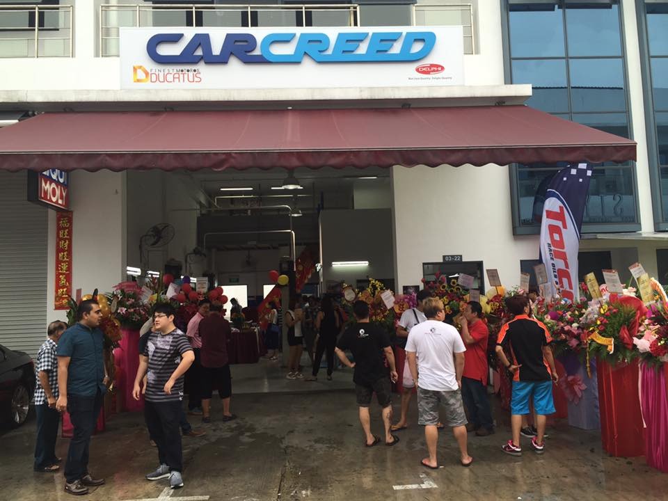 JW Motoring heritage — workshop grand opening with congratulatory floral stands and a crowd at the entrance