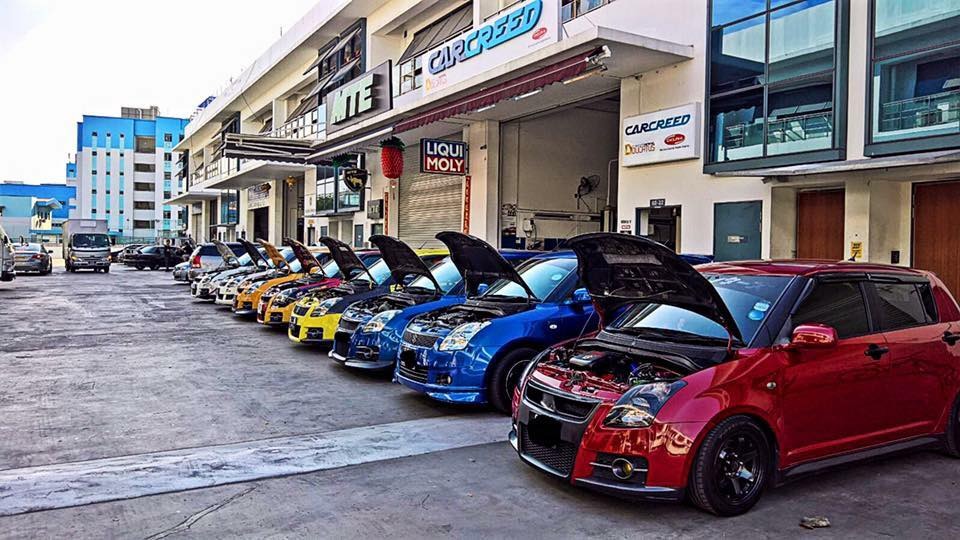 Line of modified Suzuki Swift cars with open bonnets parked outside the workshop during a car meet